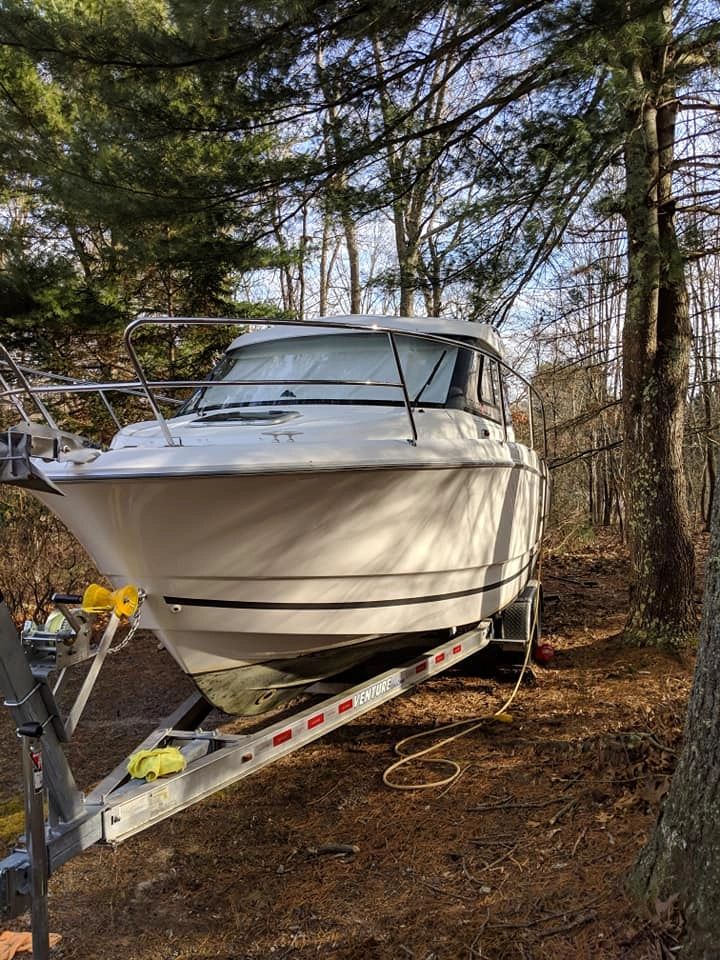 White cabin cruiser on an aluminum trailer being moved through a wooded Rhode Island property